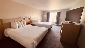 A hotel room with two beds, a desk, a TV, and a window with curtains.