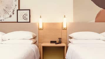 Habitación de hotel con dos camas, cabecero de madera, lámparas de noche, mesitas de noche y cuadros en la pared.