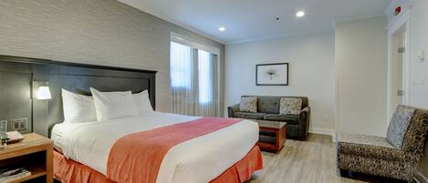 A hotel room with a large bed, a sofa, a chair, a nightstand, and a window with curtains.