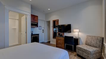 A hotel room with a large bed, a desk with a chair, a television, and a small kitchenette.