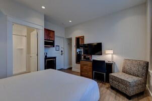 A hotel room with a large bed, a desk with a chair, a television, and a small kitchenette.