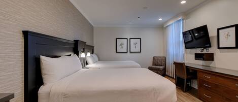 A hotel room with a large bed, a desk with a chair, a television, and framed pictures on the wall.