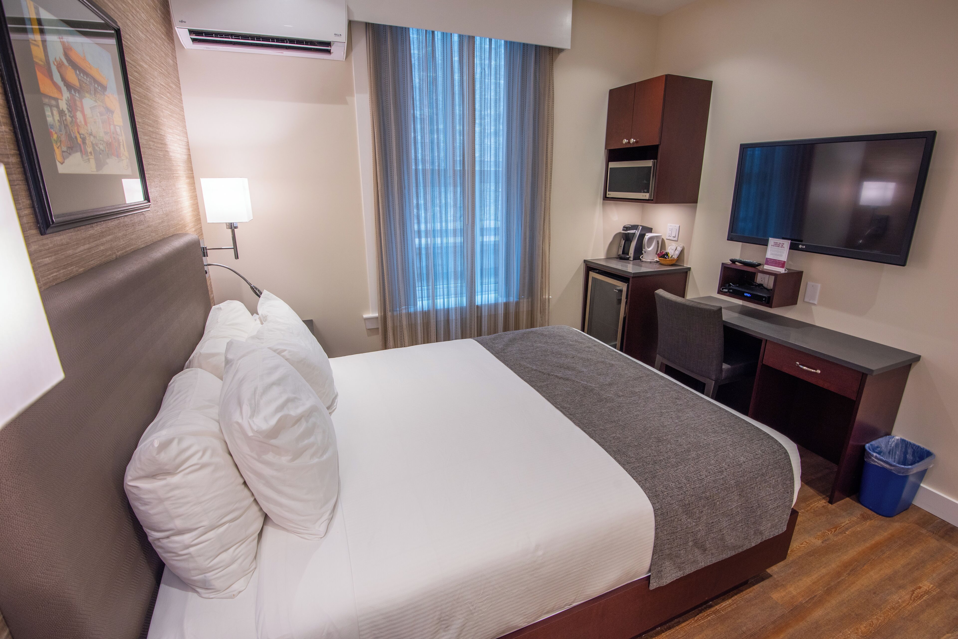 A hotel room with a bed, a desk, a television, and a window with curtains.