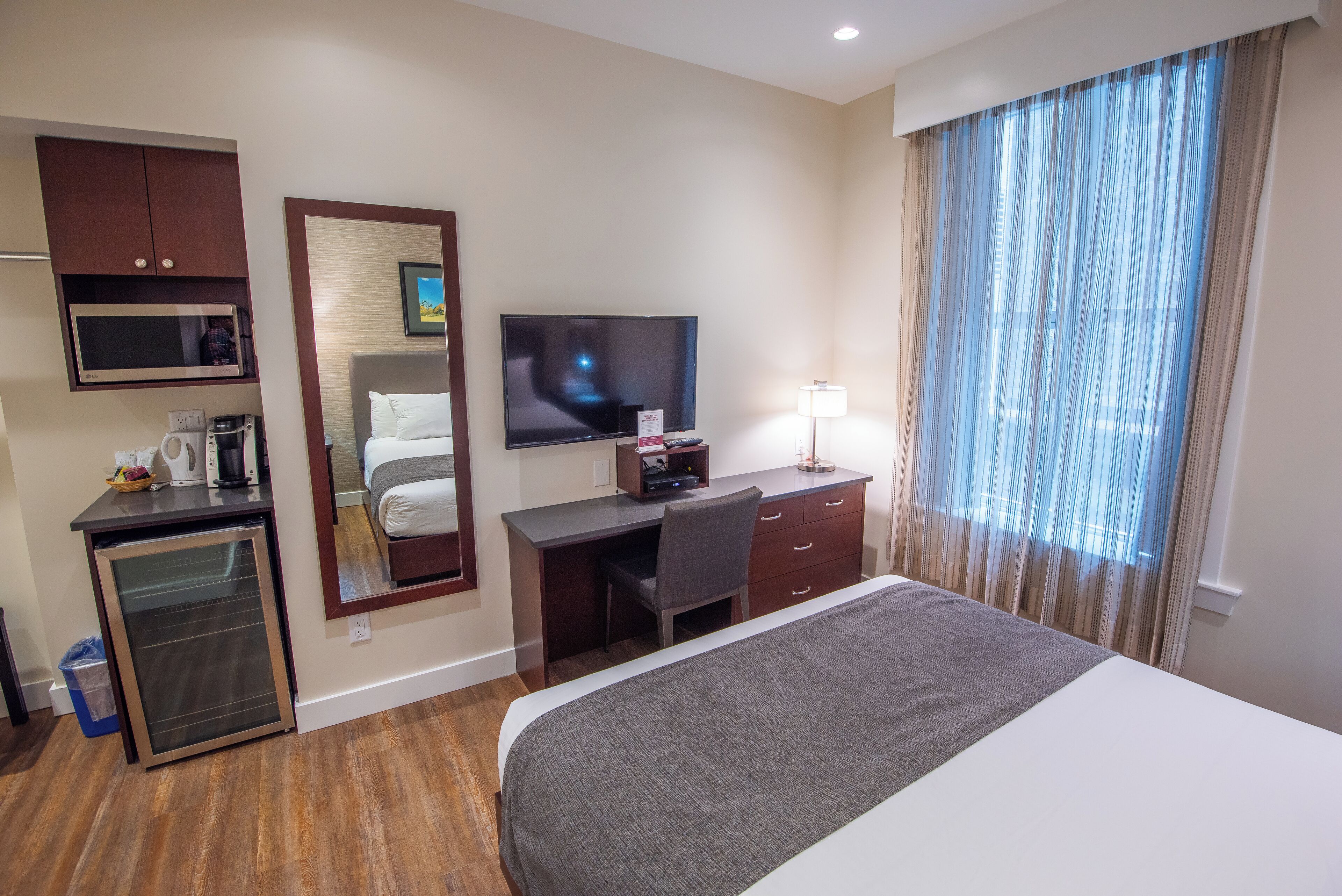 A hotel room with a bed, a desk with a computer, a television, a microwave, and a mini-fridge.