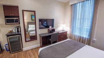 A hotel room with a bed, a desk with a computer, a television, a microwave, and a mini-fridge.
