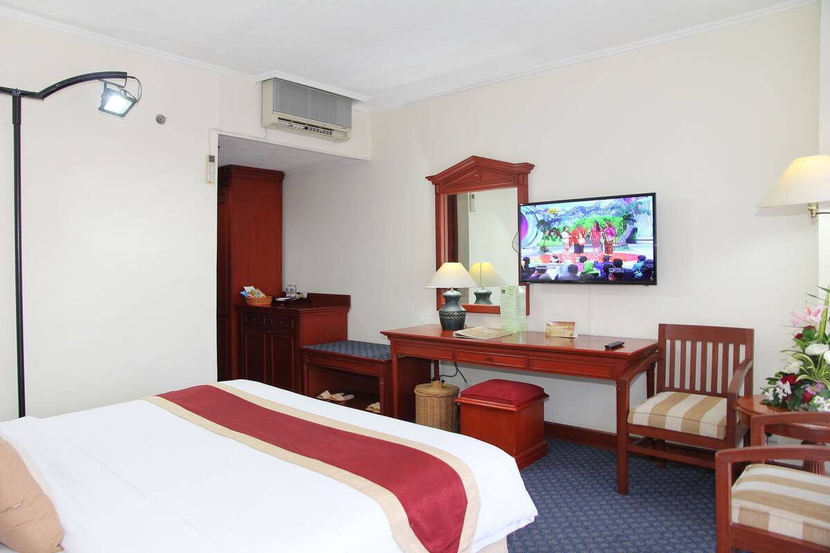A hotel room with a bed, desk, chair, television, and a mirror.