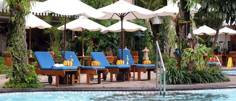 Zona de piscina con sillones reclinables y sombrillas, rodeada de exuberante vegetación.