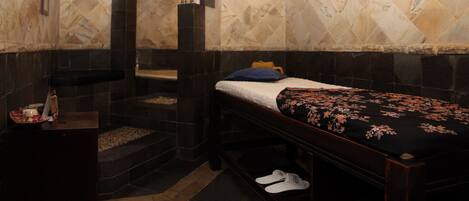 A room with a bed, a bench, a small table, and a wall-mounted light fixture.