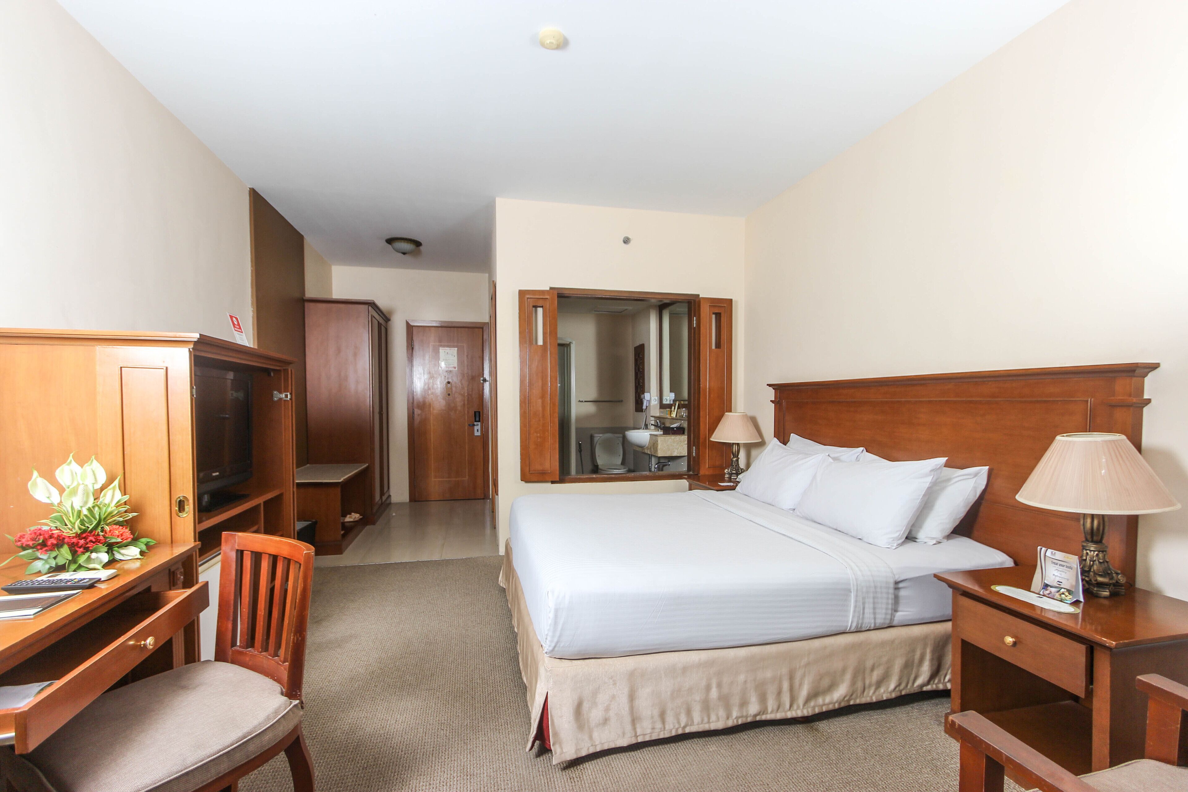 A hotel room with a bed, desk, chair, TV, and a mirror.