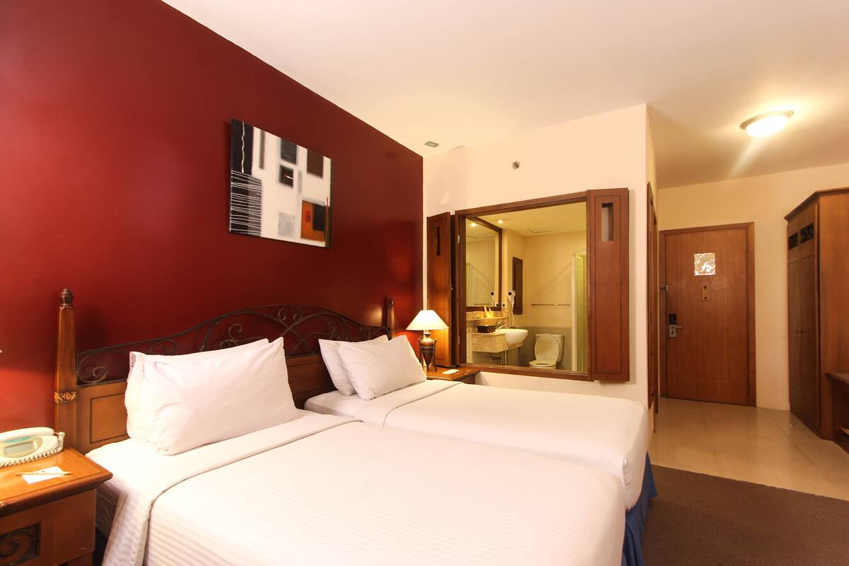 A hotel room with two beds, a wooden headboard, a bedside table with a lamp, a mirror, and a wardrobe.