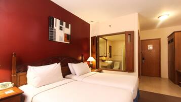 A hotel room with two beds, a wooden headboard, a bedside table with a lamp, a mirror, and a wardrobe.