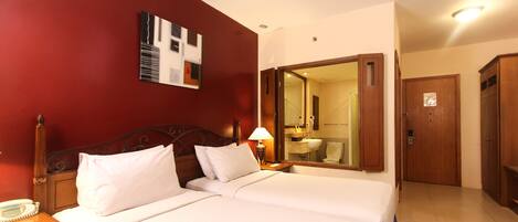 Une chambre d’hôtel avec deux lits, une tête de lit en bois, une table de chevet avec une lampe, un miroir et une armoire.