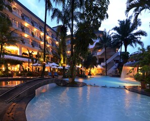 Un hôtel doté d’une piscine, de palmiers et d’une cascade.