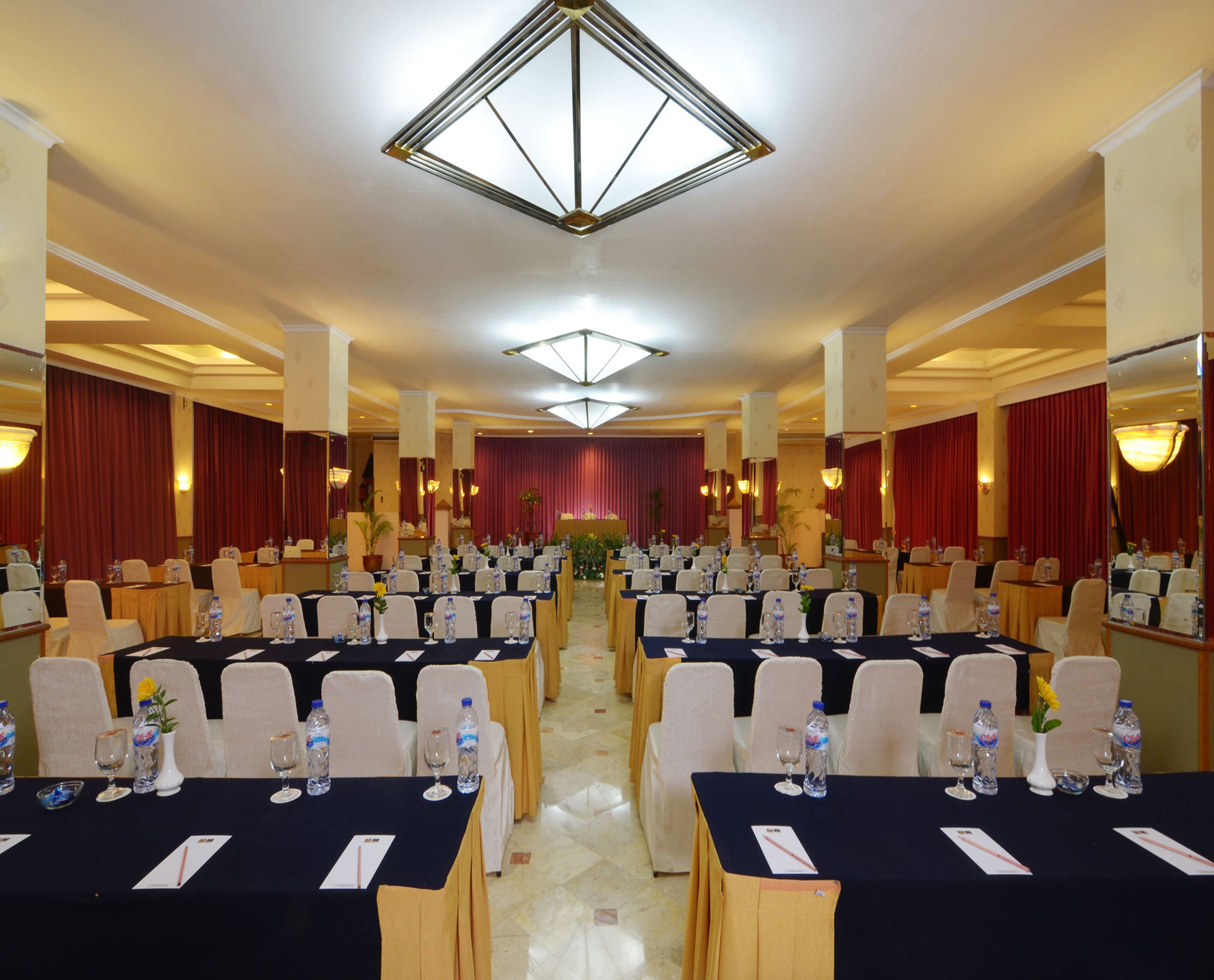 A conference room with multiple tables, chairs, and a stage with curtains.