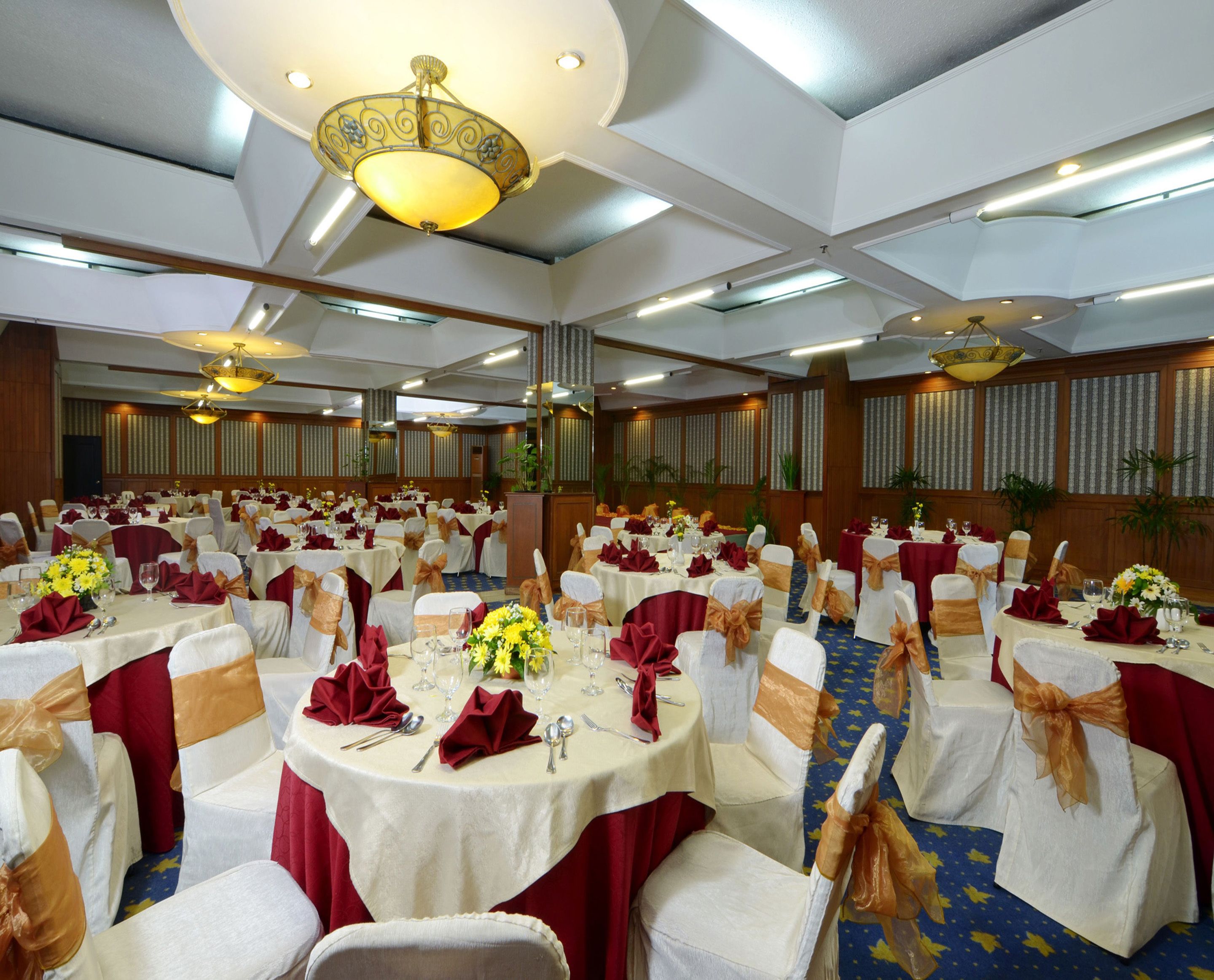 A banquet hall with round tables, white tablecloths, and chairs with red and gold sashes.