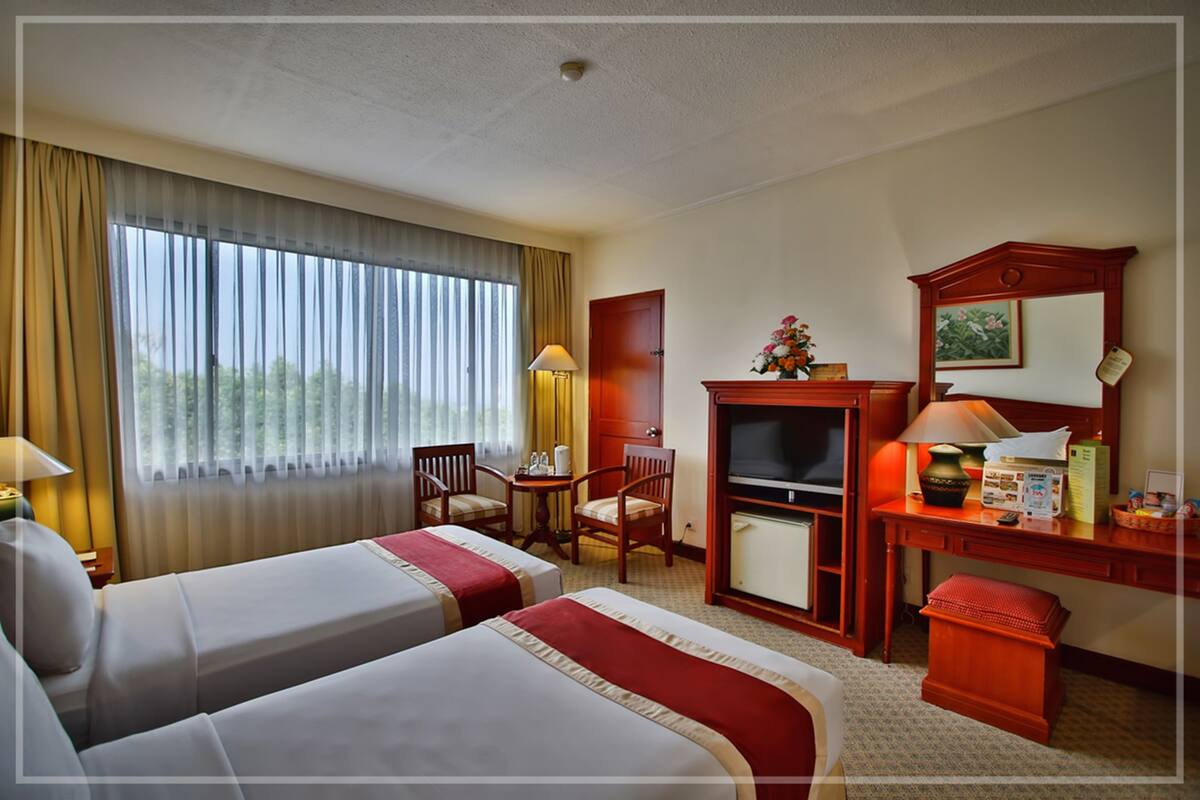 A hotel room with two beds, a desk, a television, and a window with curtains.