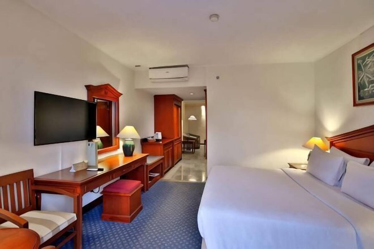 A hotel room with a bed, a desk with a chair, a television, and a lamp.