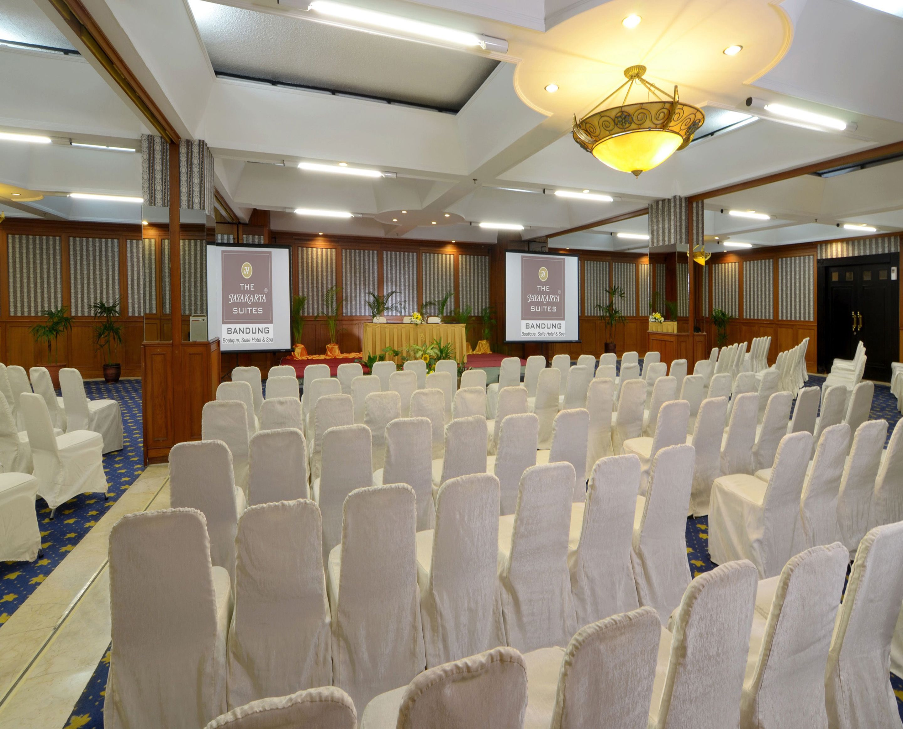 A conference room with rows of white chairs, a stage with a banner, and a chandelier.