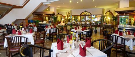 A spacious dining area with multiple tables set for dining, featuring red napkins and white tablecloths.