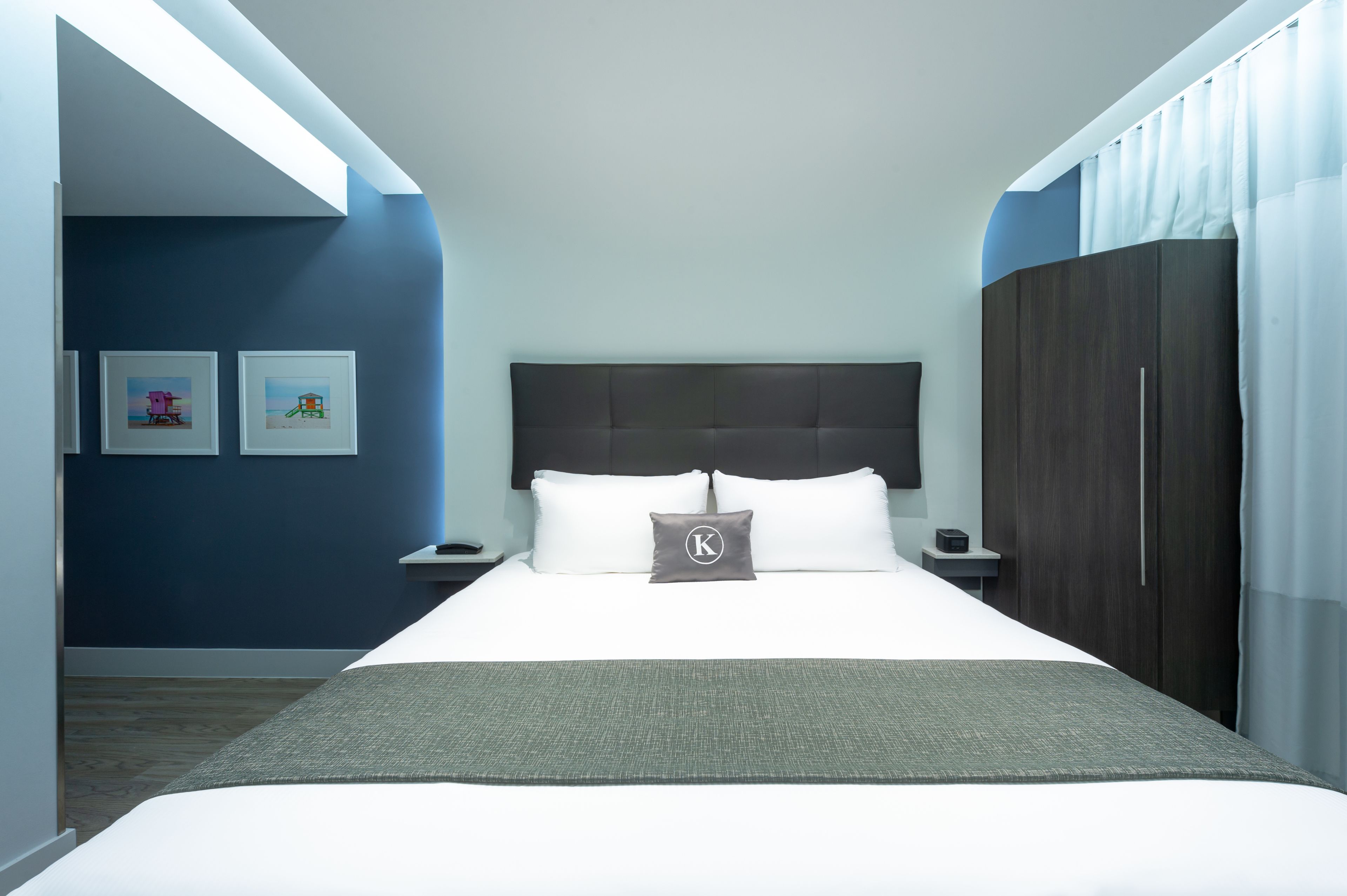 Une chambre d’hôtel moderne avec un grand lit, une tête de lit sombre et une table de chevet avec un téléphone.