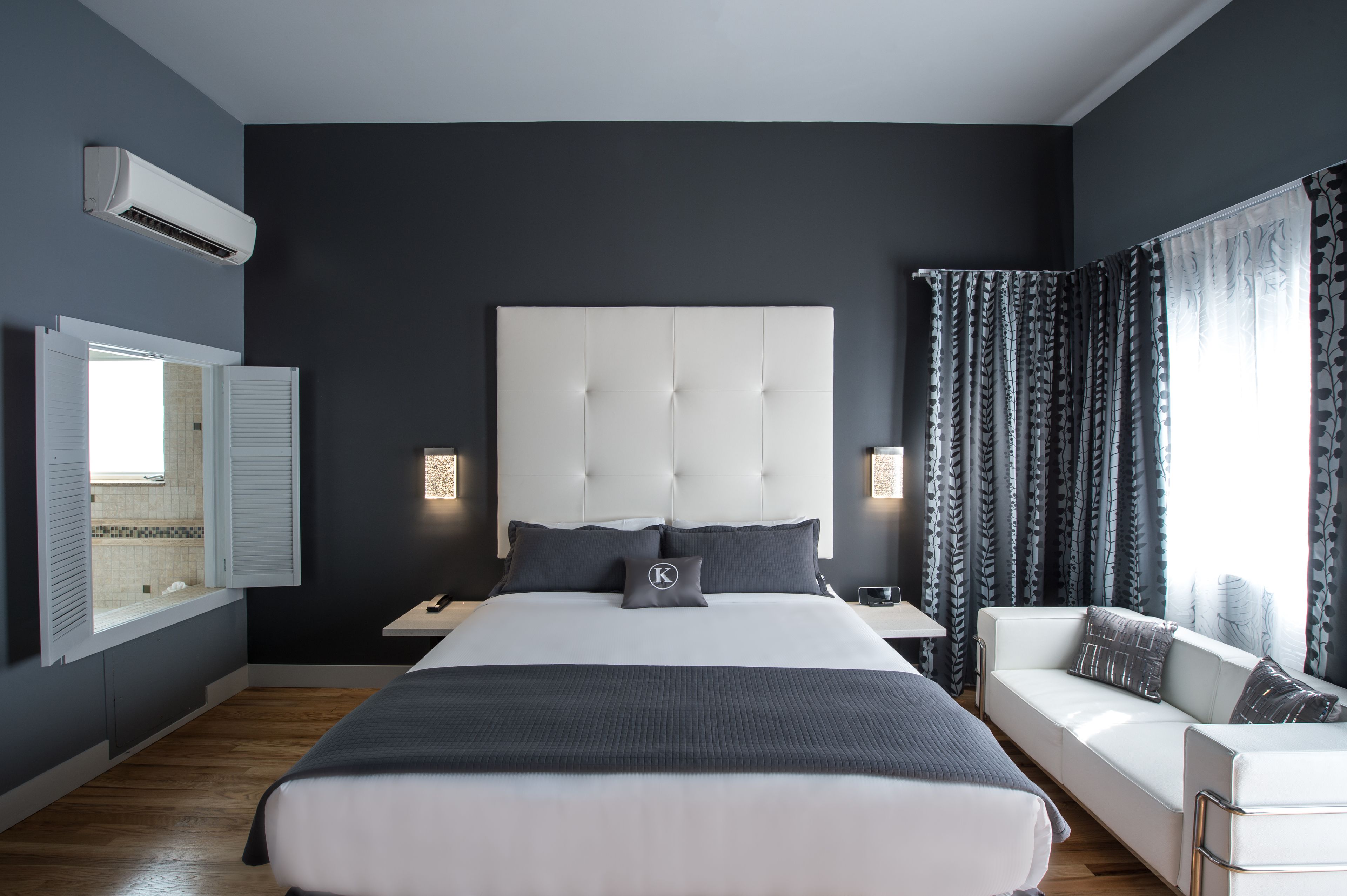 A modern bedroom with a large bed, bedside tables, a white sofa, and a window with curtains.