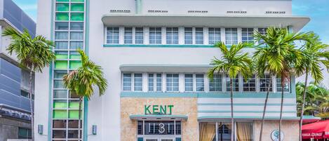 A modern hotel with a prominent 'KENT' sign, large windows, and palm trees in front.