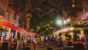 An outdoor market with people walking and dining under palm trees and string lights. - The Kent Hotel (Miami Beach)