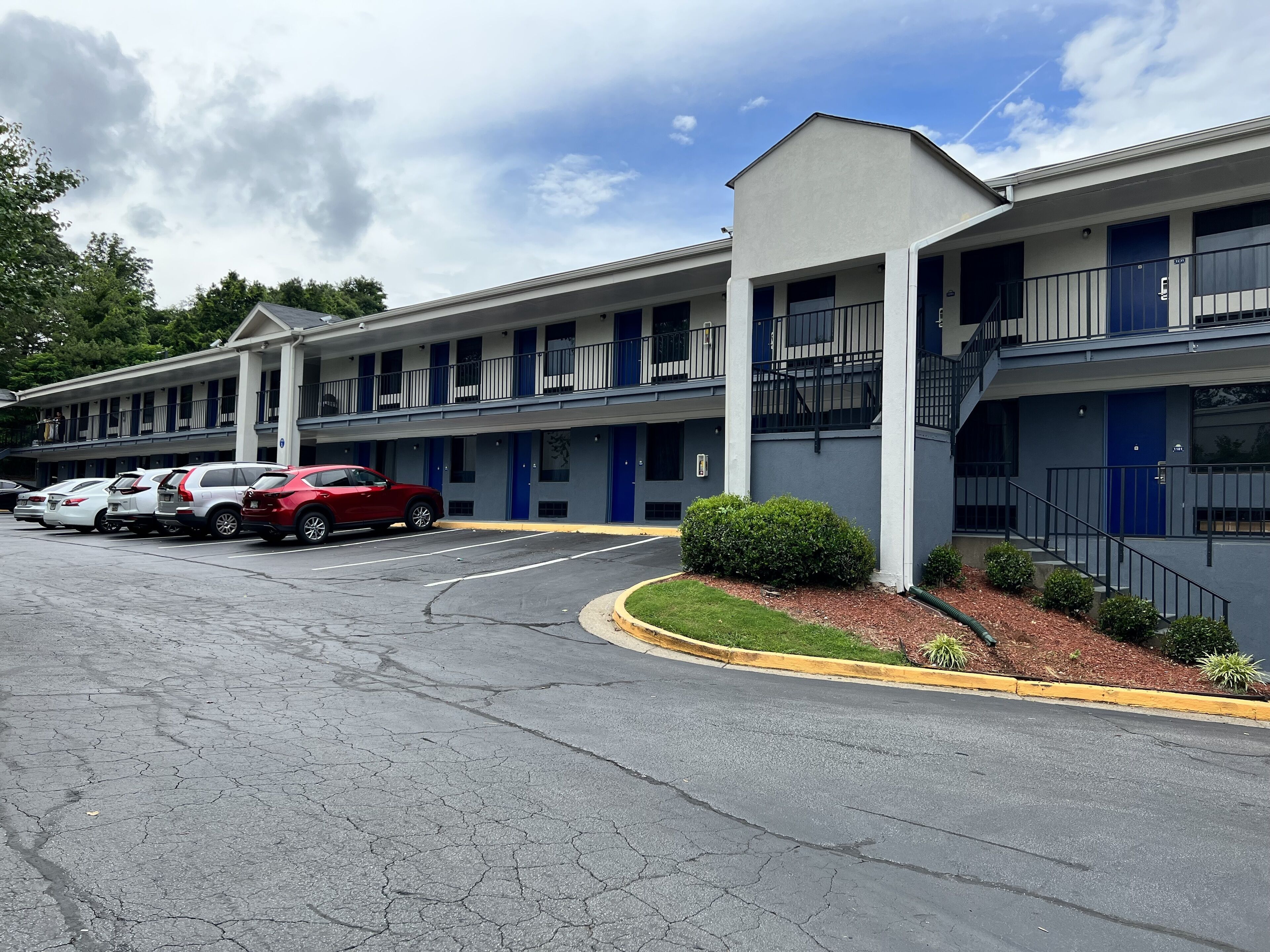 A motel with multiple floors, a parking lot with several cars, and a well-maintained lawn area.