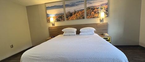 A neatly made bed with a white comforter and pillows, a wooden headboard, two bedside tables with lamps, and three framed landscape paintings on the wall.