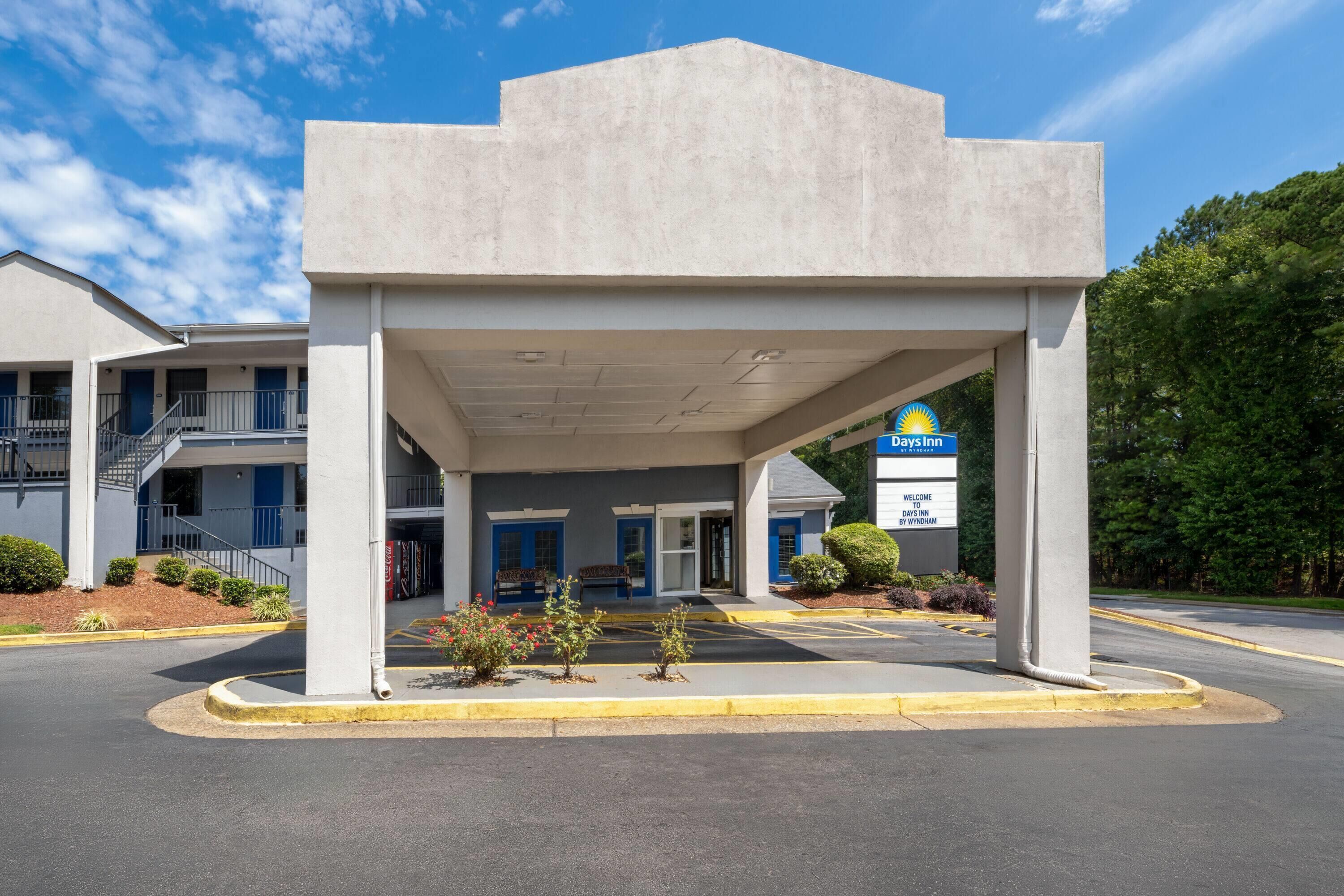 A Days Inn by Wyndham with a covered entrance, a parking lot, and a building with blue doors.