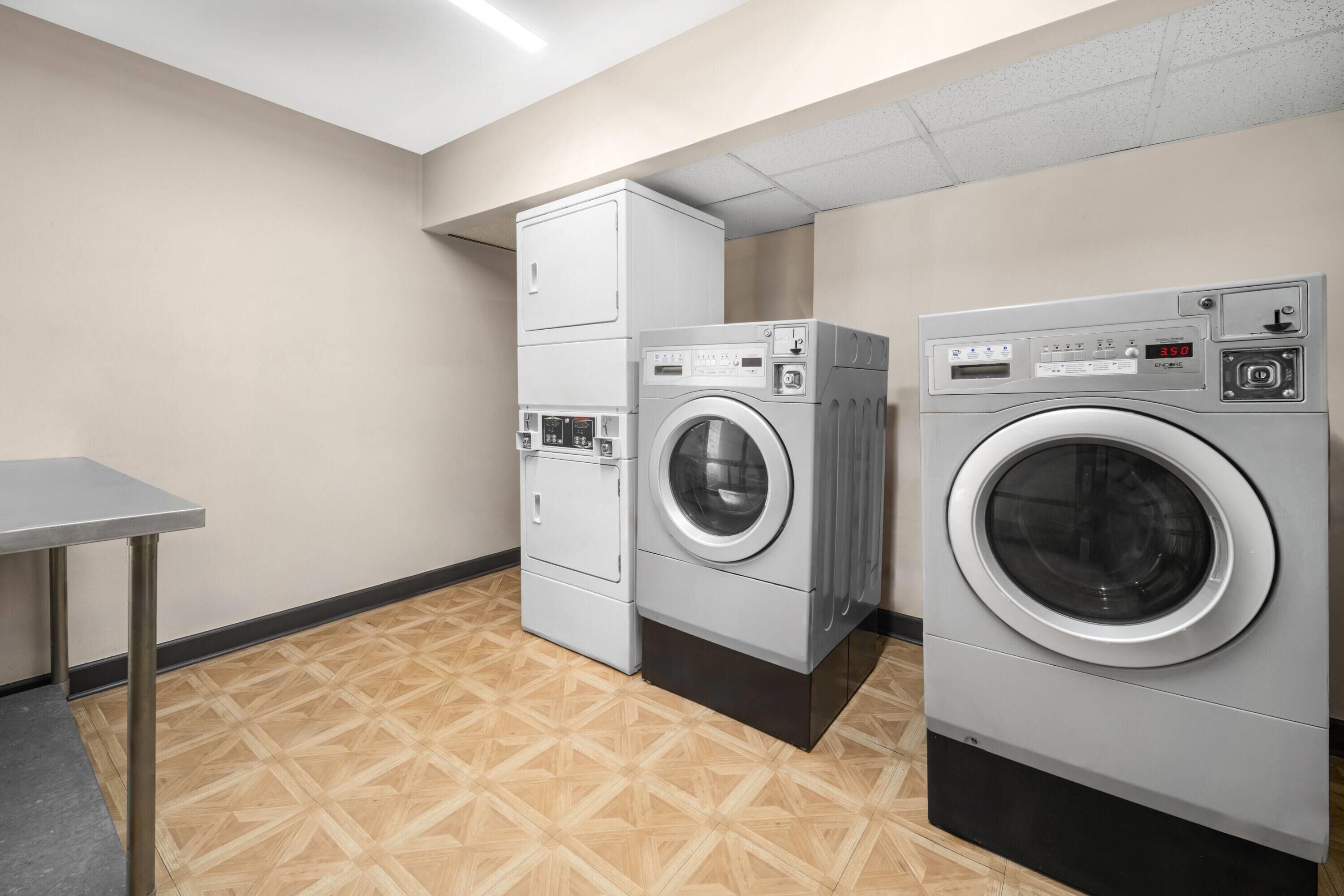 A laundry room with two stacked washers and dryers, a metal table, and a patterned floor.