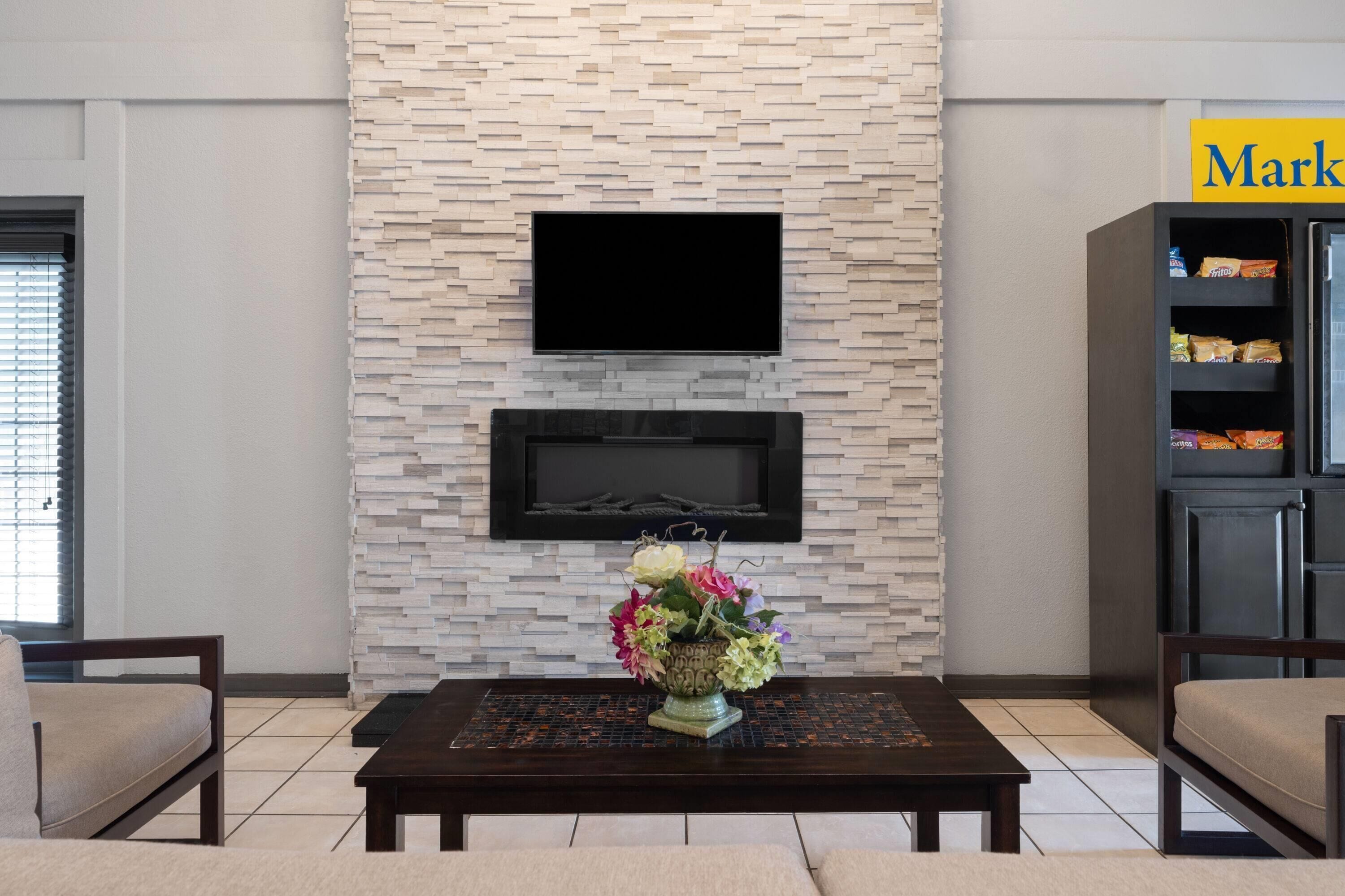 A modern living room with a stone-patterned wall, a flat-screen TV, a fireplace, and a coffee table with a floral arrangement.