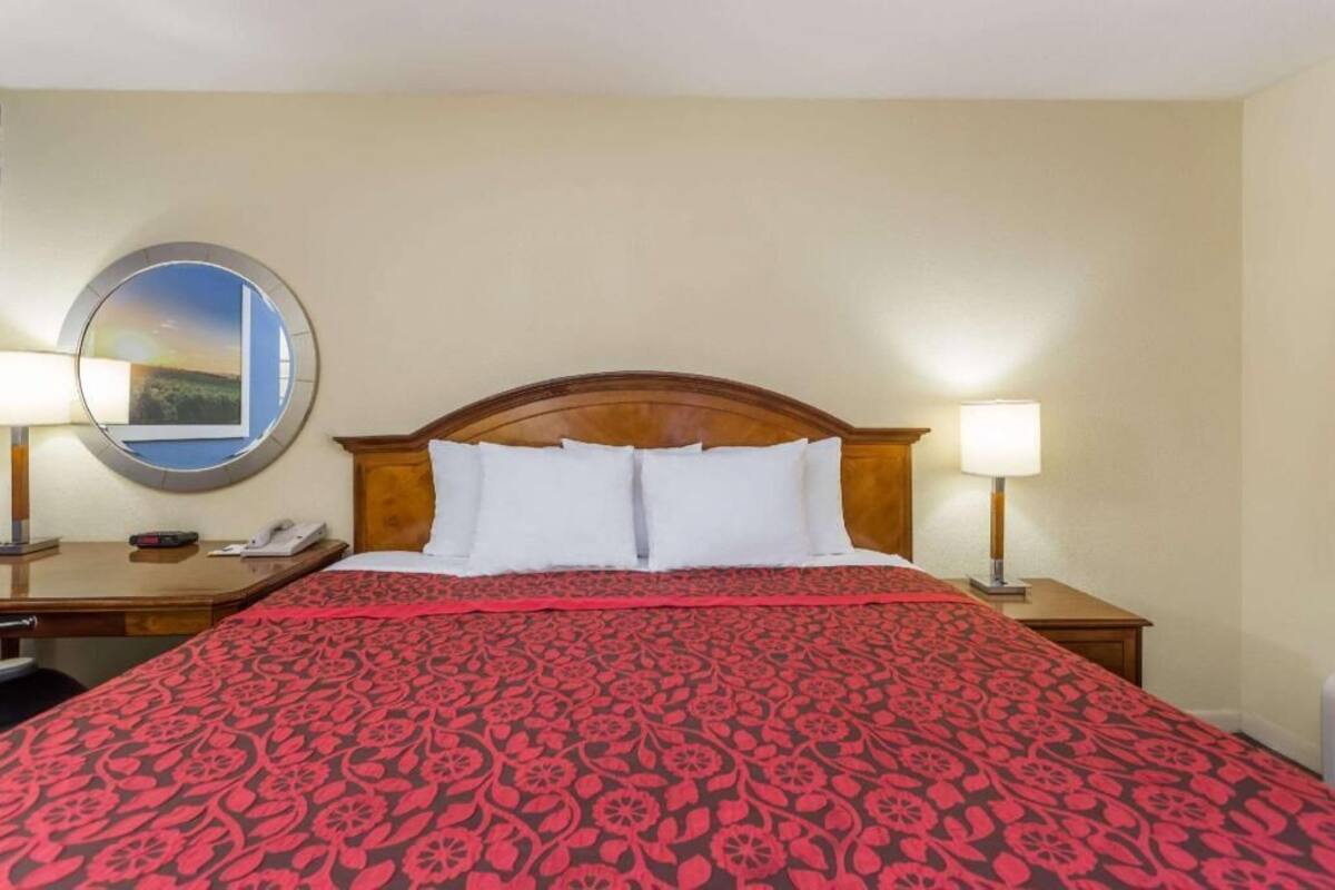Habitación de hotel con una cama grande, dos mesitas de noche, un espejo redondo y vistas al cielo.