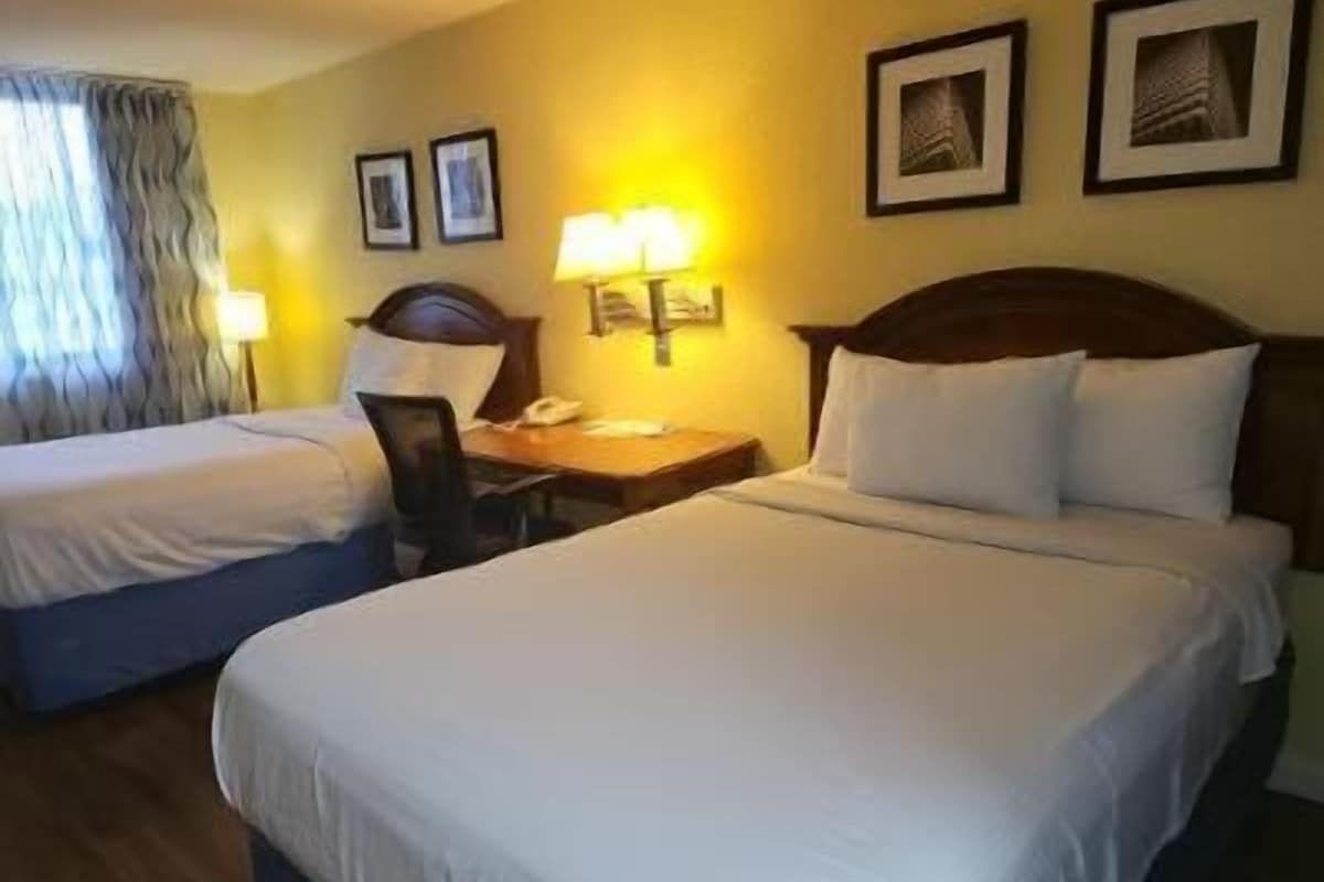 A hotel room with two beds, a desk, a lamp, and framed pictures on the wall.