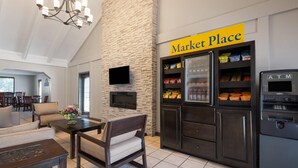 Un hall d’hôtel avec un mur en pierre, une enseigne indiquant « Market Place », un distributeur automatique de billets et des espaces aménagés avec des sièges.