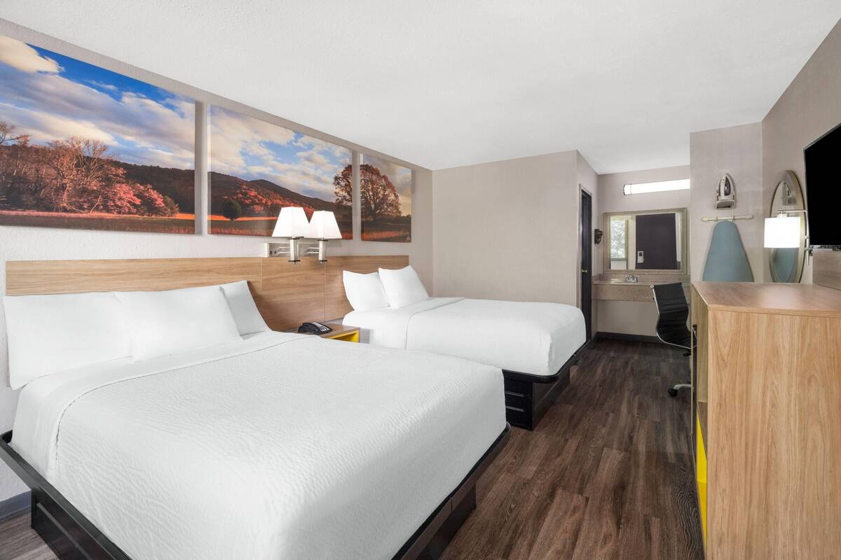 Habitación de hotel con dos camas, un escritorio, una silla, un espejo y un ventanal con vistas panorámicas.
