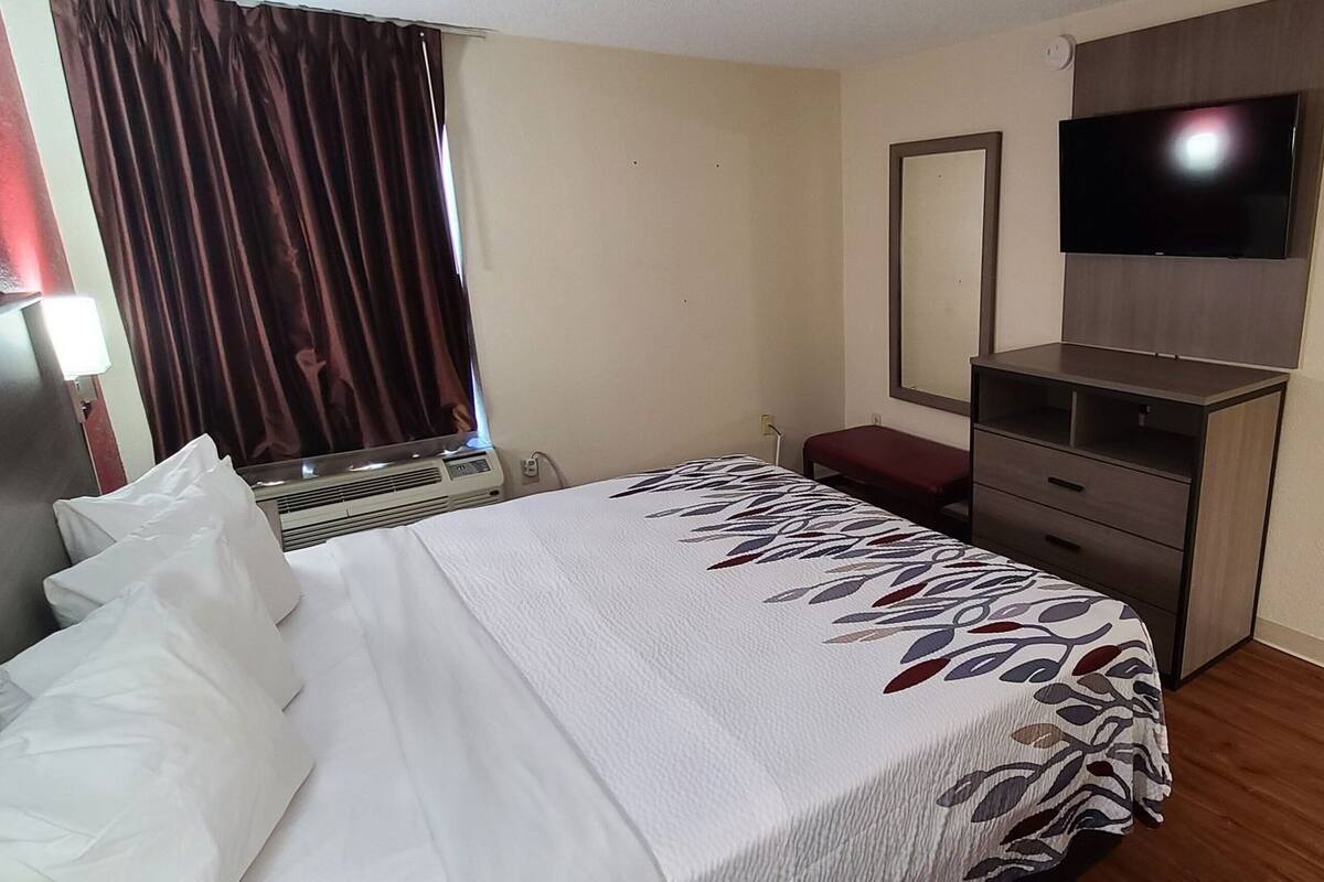 Habitación de hotel con cama, televisor montado en la pared, escritorio y espejo.