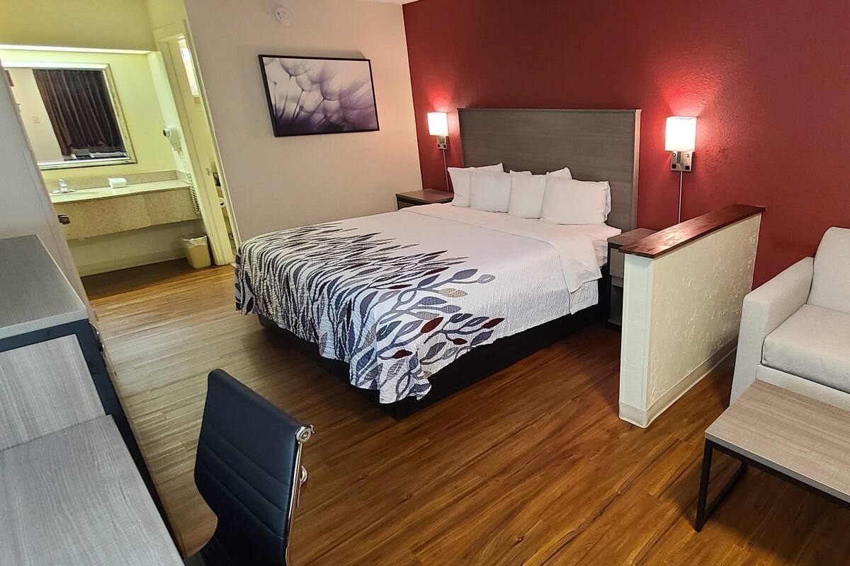 Una habitación de hotel con cama, una silla, un escritorio y una mesita de noche.