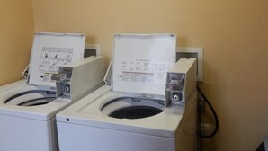 Two front-loading washing machines with instruction manuals, set against a plain wall. - Red Roof Inn & Suites Cornelius – Lake Norman (Cornelius)