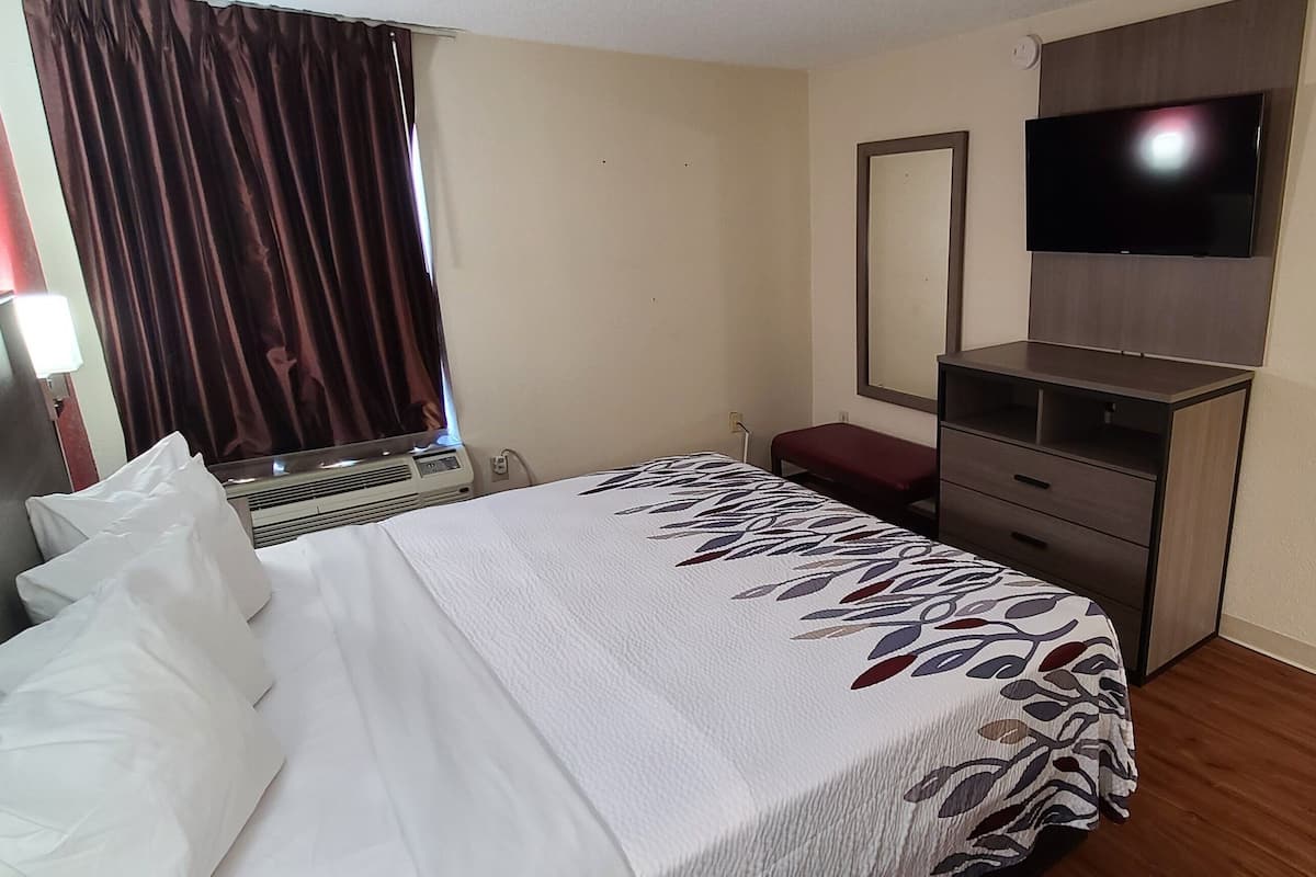Una habitación de hotel con una cama, un televisor en la pared, un aparador y un espejo.