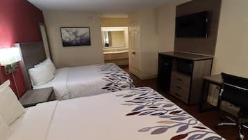 Habitación de hotel con dos camas, un escritorio, una silla, un televisor y un baño a la vista.