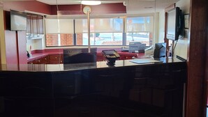 A reception desk with a computer, a cash register, and a window with a view of the outside. - Red Roof Inn & Suites Cornelius – Lake Norman (Cornelius)