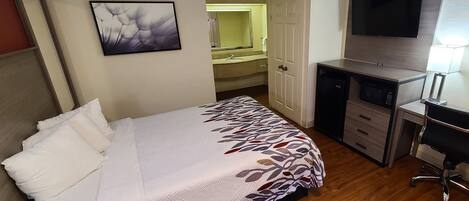 A hotel room with a bed, a desk, a TV, and a bathroom.