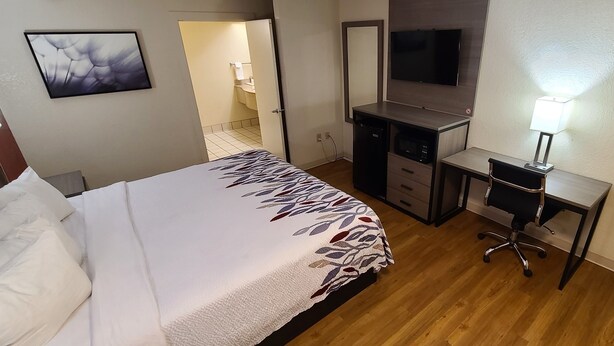 Habitación de hotel con cama, escritorio, silla, televisor y baño visible a través de una puerta abierta.