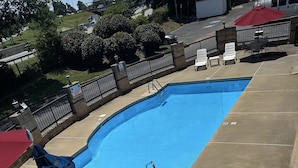 A swimming pool with lounge chairs and umbrellas, surrounded by a fence and greenery. - Red Roof Inn & Suites Cornelius – Lake Norman (Cornelius)