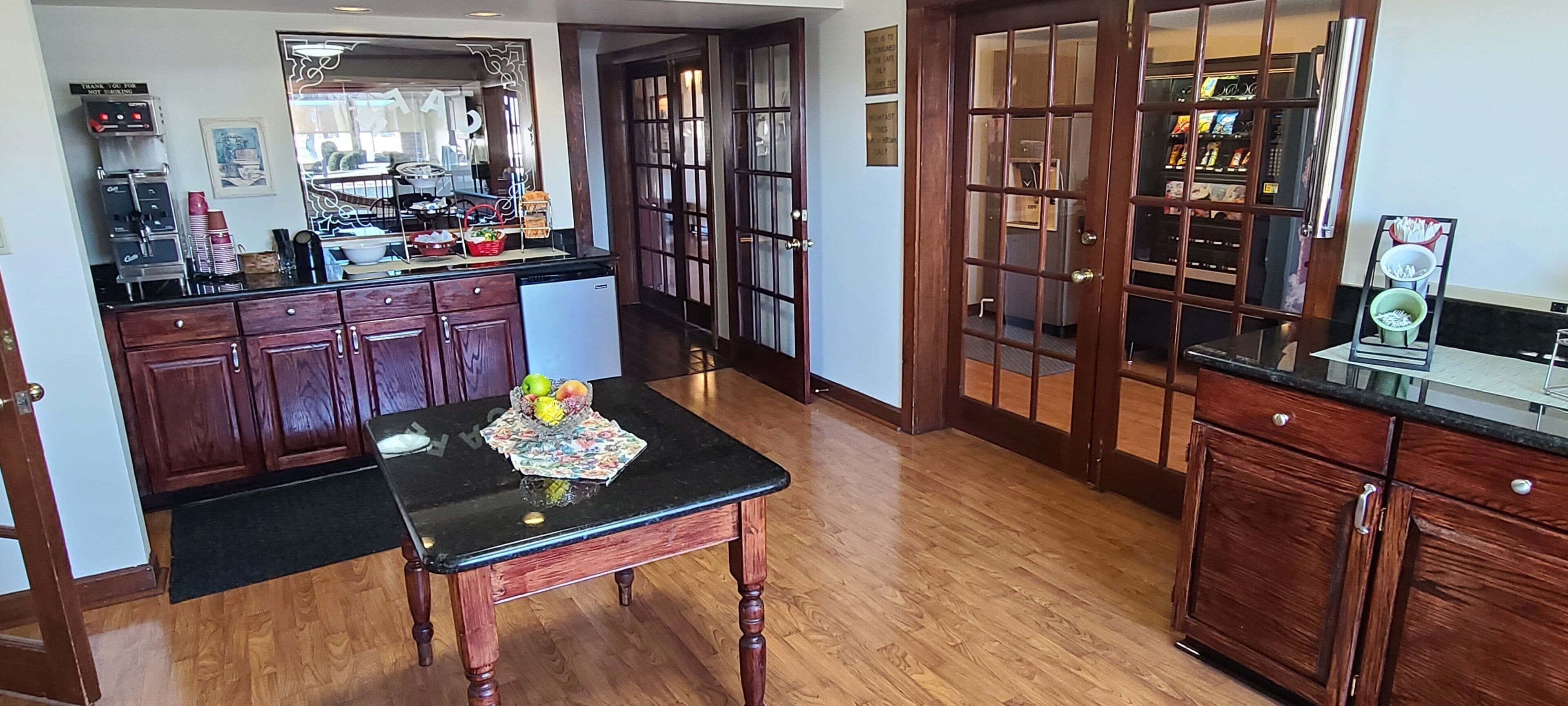 A kitchen with wooden cabinets, a black countertop, and a dining table with fruits.