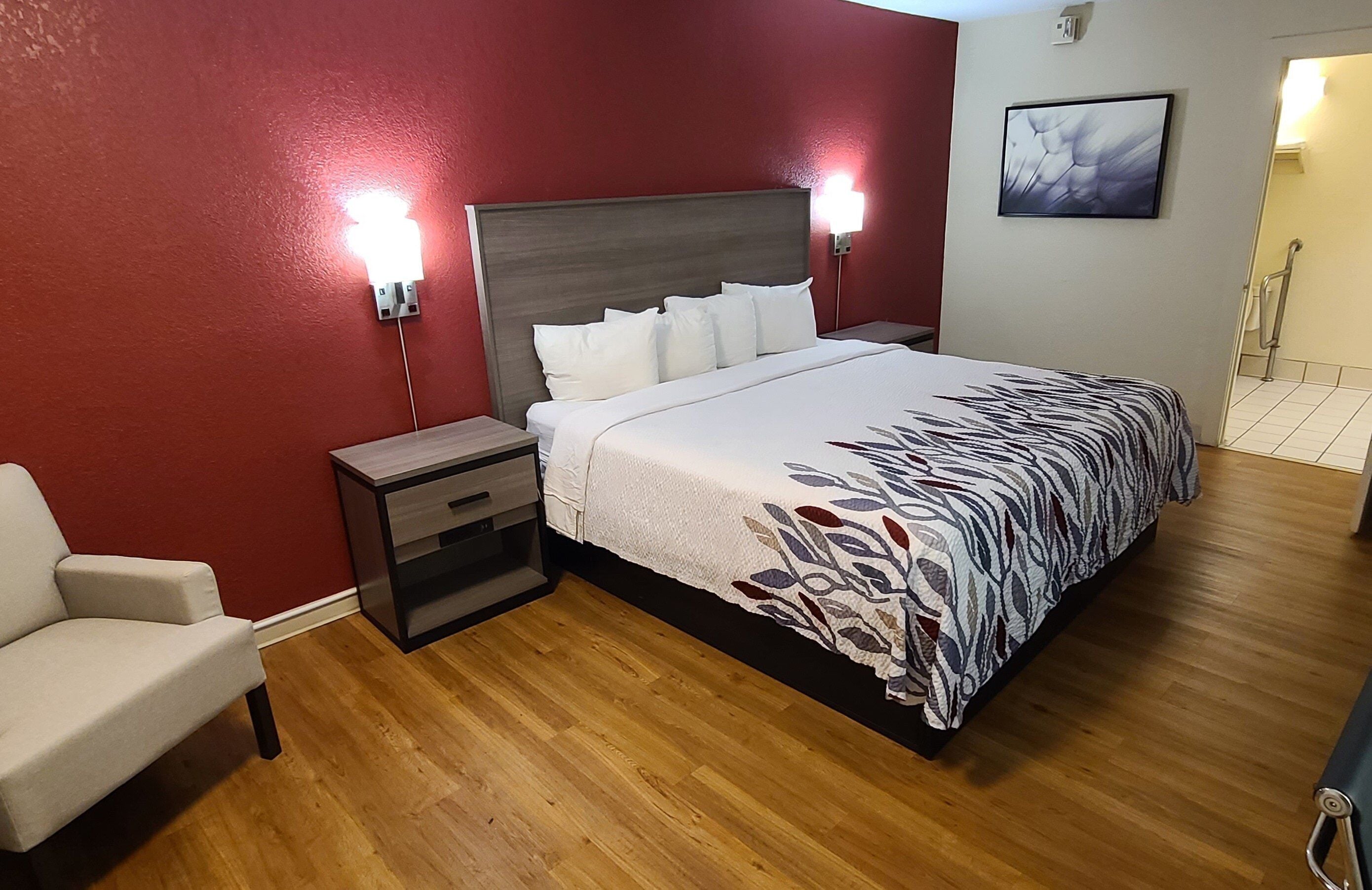 A hotel room with a bed, bedside tables, a chair, and a wall-mounted artwork.
