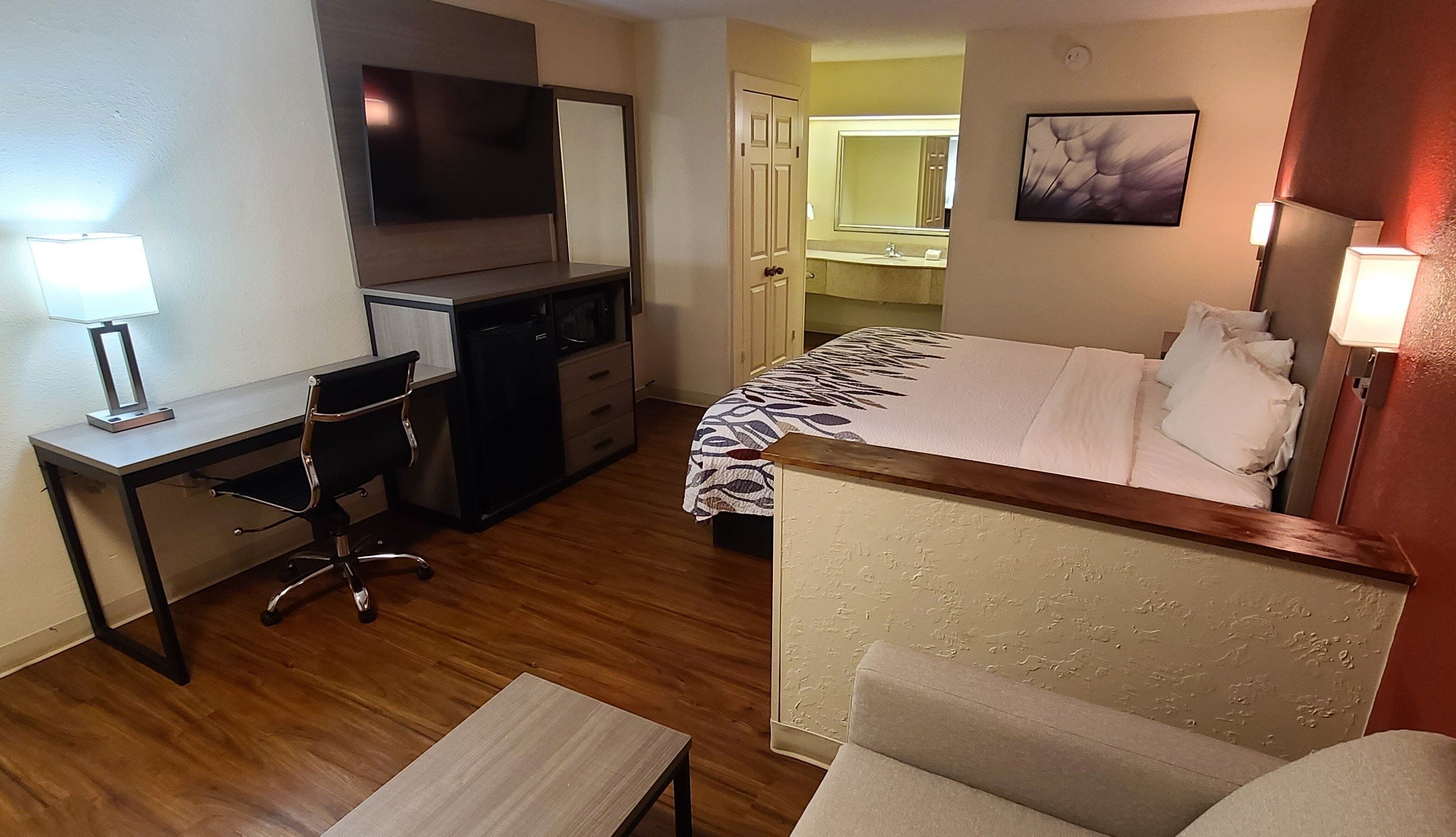 A hotel room with a bed, desk, chair, and a television.