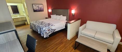 A hotel room with a bed, a chair, a bedside table, and a wall-mounted light.