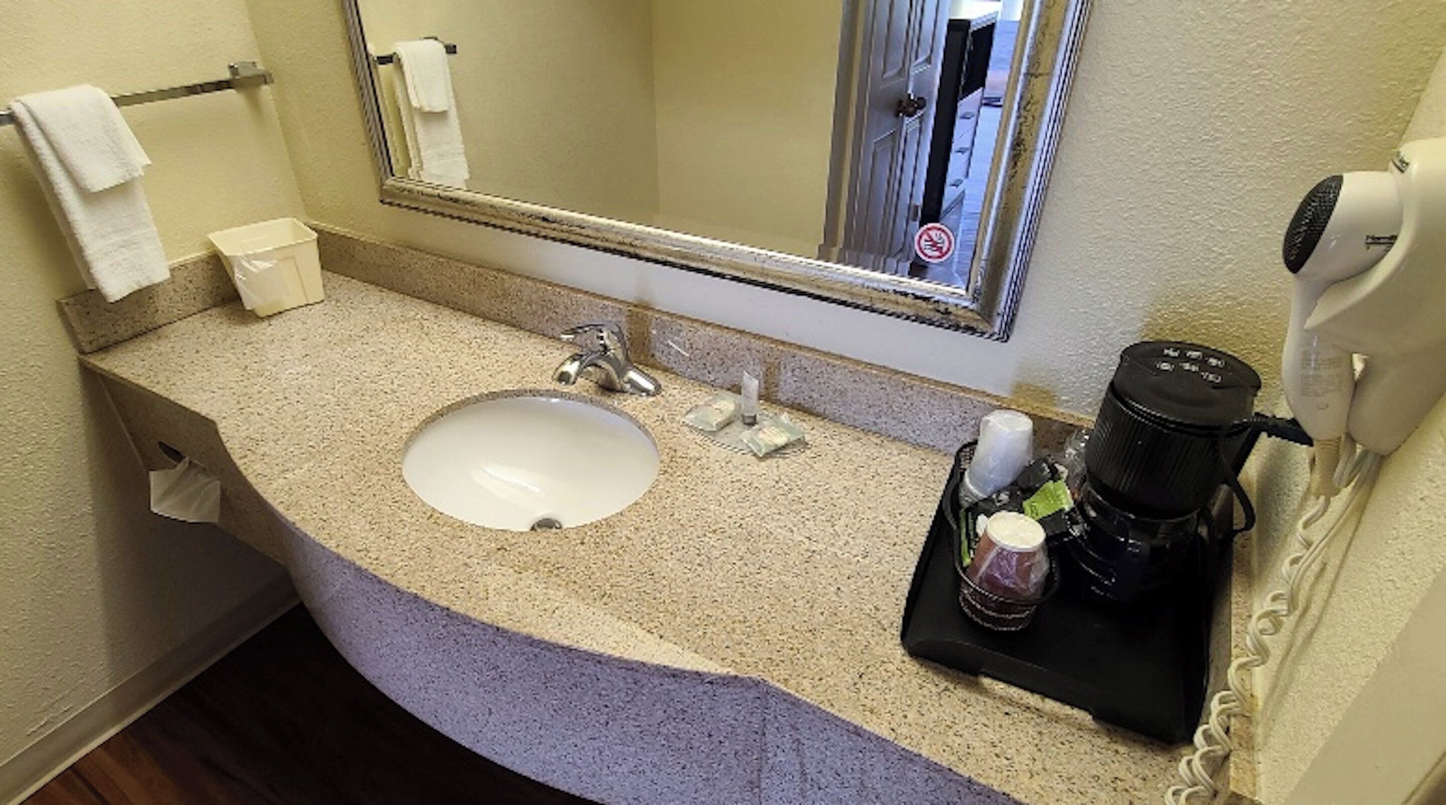 Un baño de hotel con lavamanos, espejo, toallero y un secador de pelo sobre una bandeja.